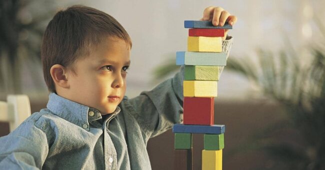 Дете учи чрез действия как се реди кула от кубчета