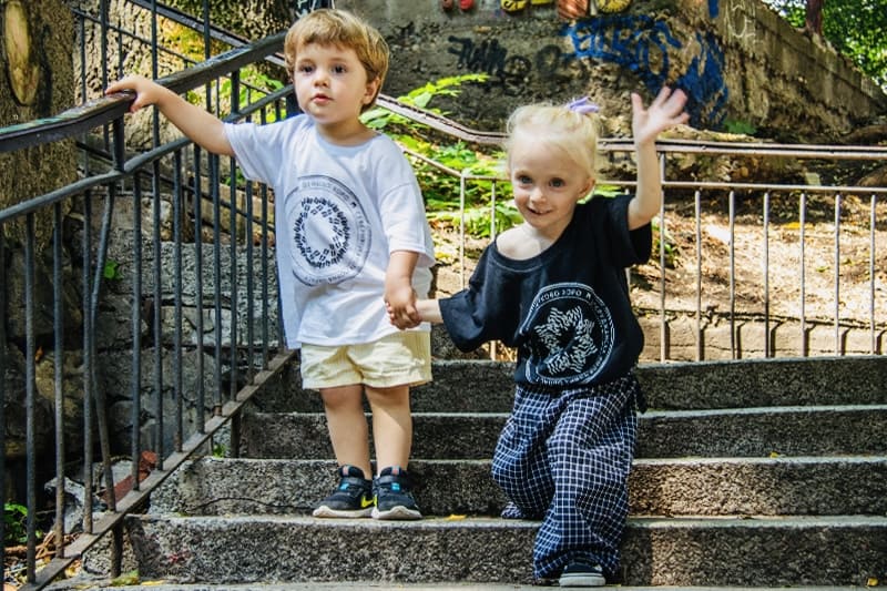 Две деца се държат за ръка и носят тениски с български хора